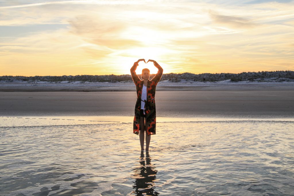 A woman holding up her arms in the shape of a heart during a sunset along the gulf of Mexico.