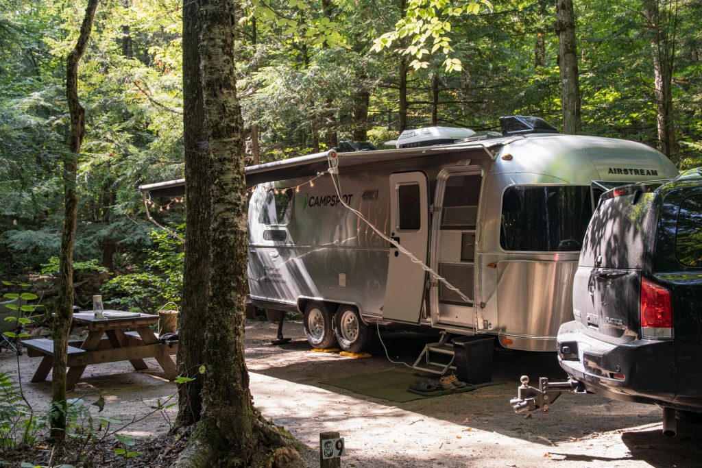 An Airstream trailer sits at campsite surrounded by lush green trees.