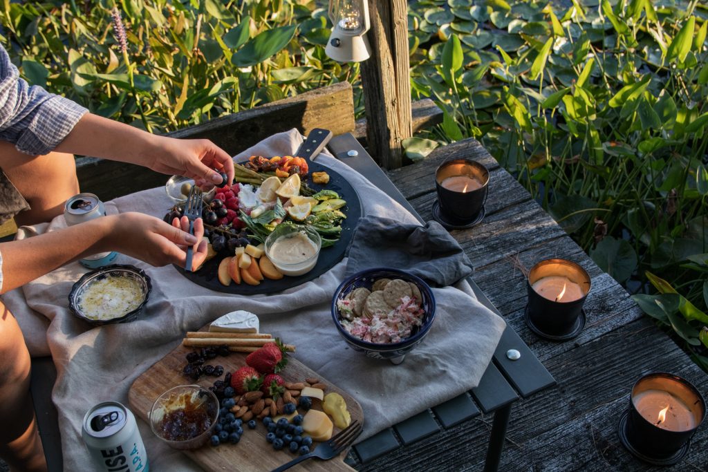 A woman picks from a cheese and charcuterie plate atop a dock surrounded by lily pads.