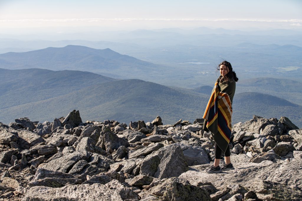 A woman wrapping herself in a Pendleton blanket on top of Mount Washington in New Hampshire.