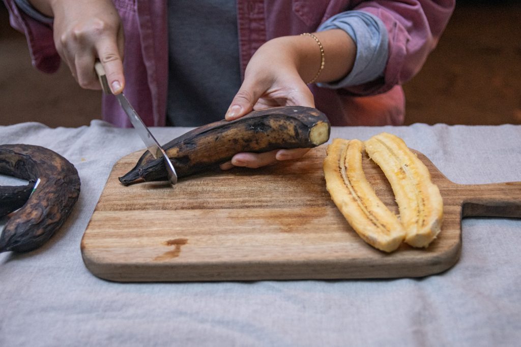 A person cuts the tips off of the plantains in preparation to slice the peel to open it.