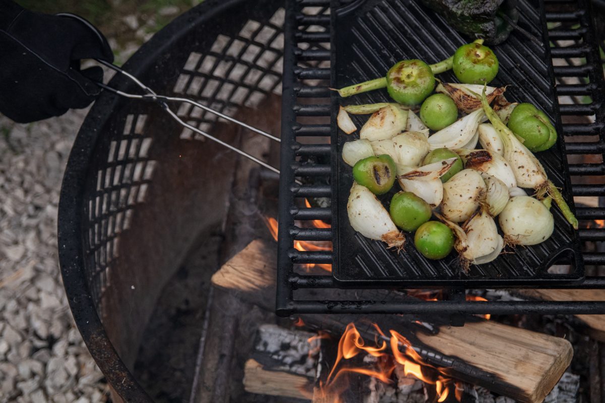 Someone is tending to grilled tomatillos and onions over a campfire.