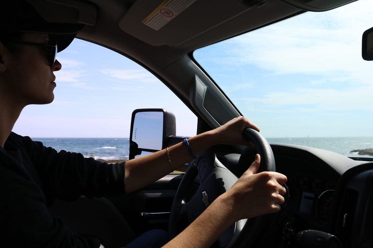 A woman driving a car along the ocean with her hands on the wheel.