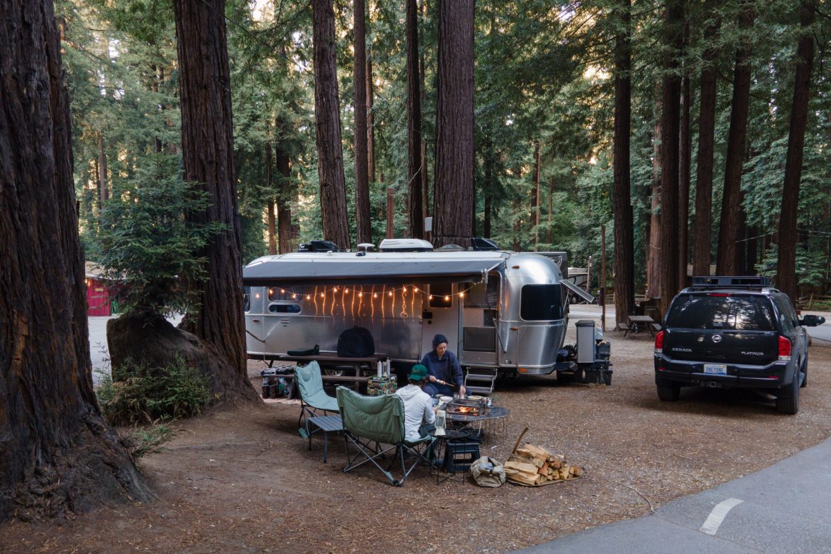 A couple sits in front of their Airstream trailer cooking a meal over their campfire at the Santa Cruz Redwoods RV Resort in Felton, California.