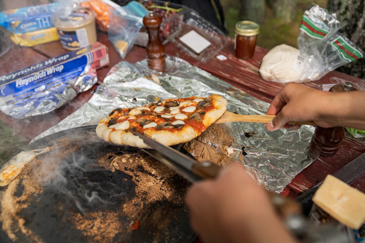 A person pulls a pizza off of a pizza peel and onto aluminum foil while making camfire pizzas.