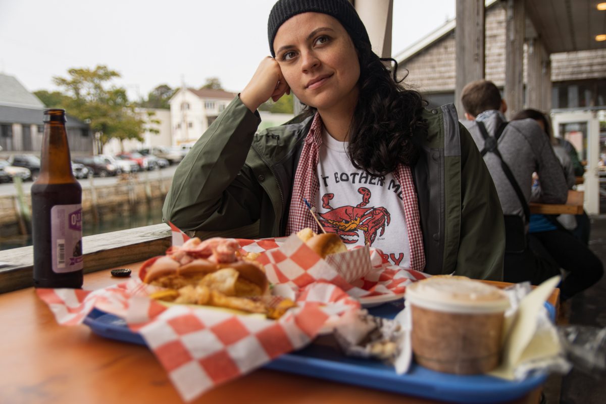 A woman sits behind a platter full of lobster rolls, blueberry pie, and clam chowder at Beal's Lobster Dock in Southwest Harbor, Maine.