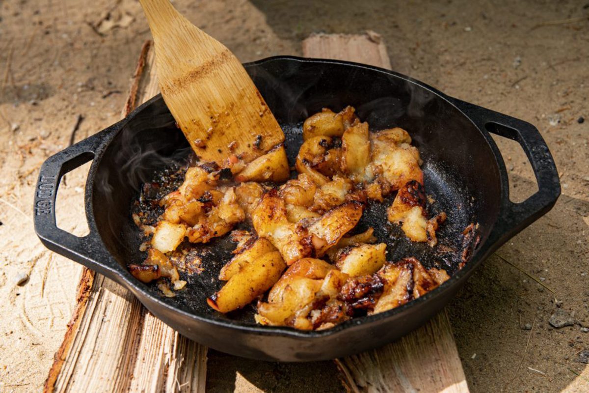 Apple bourbon topping and cast iron skillet cools on two logs. 