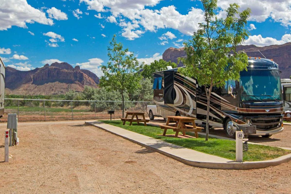 An Rv parked near a picnic table with a mountain view in the background at Sun Outdoors Arches Gateway in Moab, UT. 