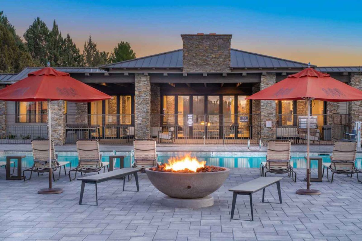 A pool with a fire pit and two red umbrellas and lounge chairs. 