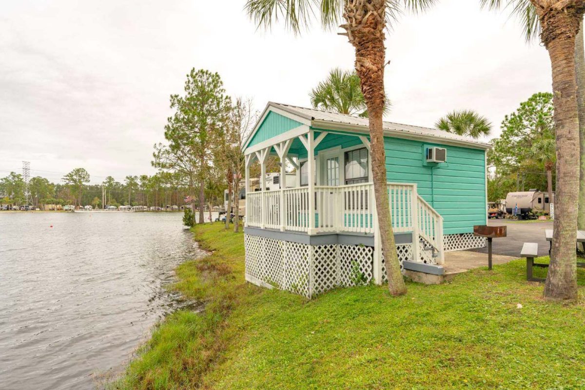 A bright colorful cabin with aquamarine siding on the water at Flamingo Lake RV Resort. 