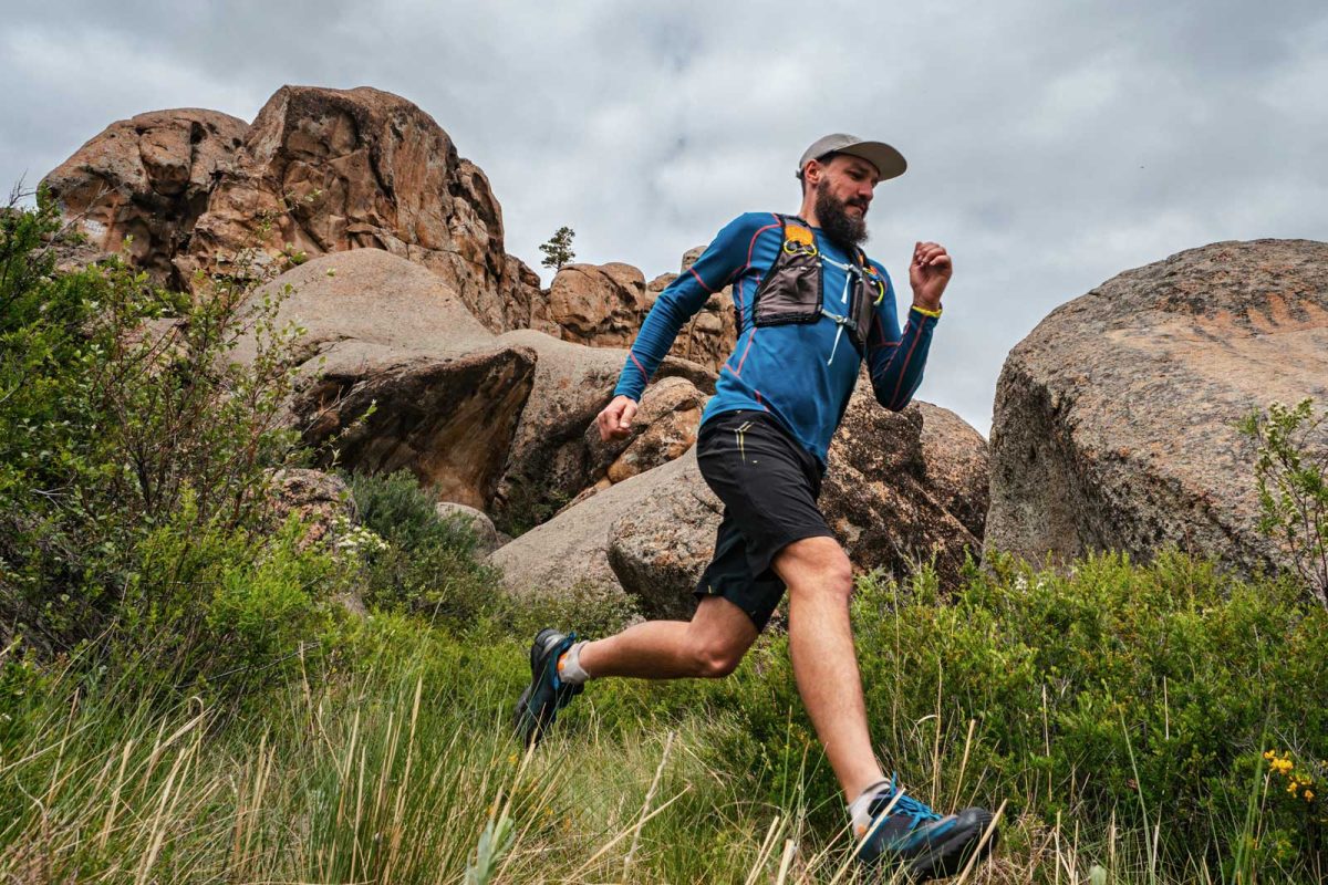 A trail runner takes the downhill wearing a long-sleeved shirt and a trail running gear pack. 