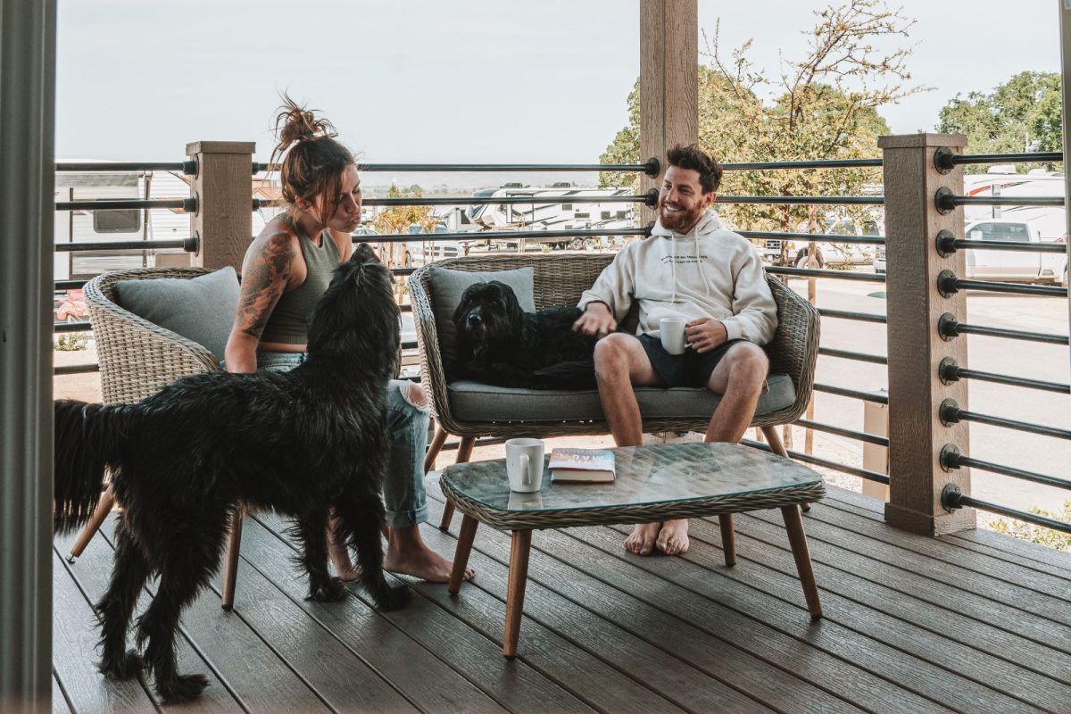 Two campers drink coffee and lounge with their dogs on a cabin patio at Sun Outdoors Paso Robles. 