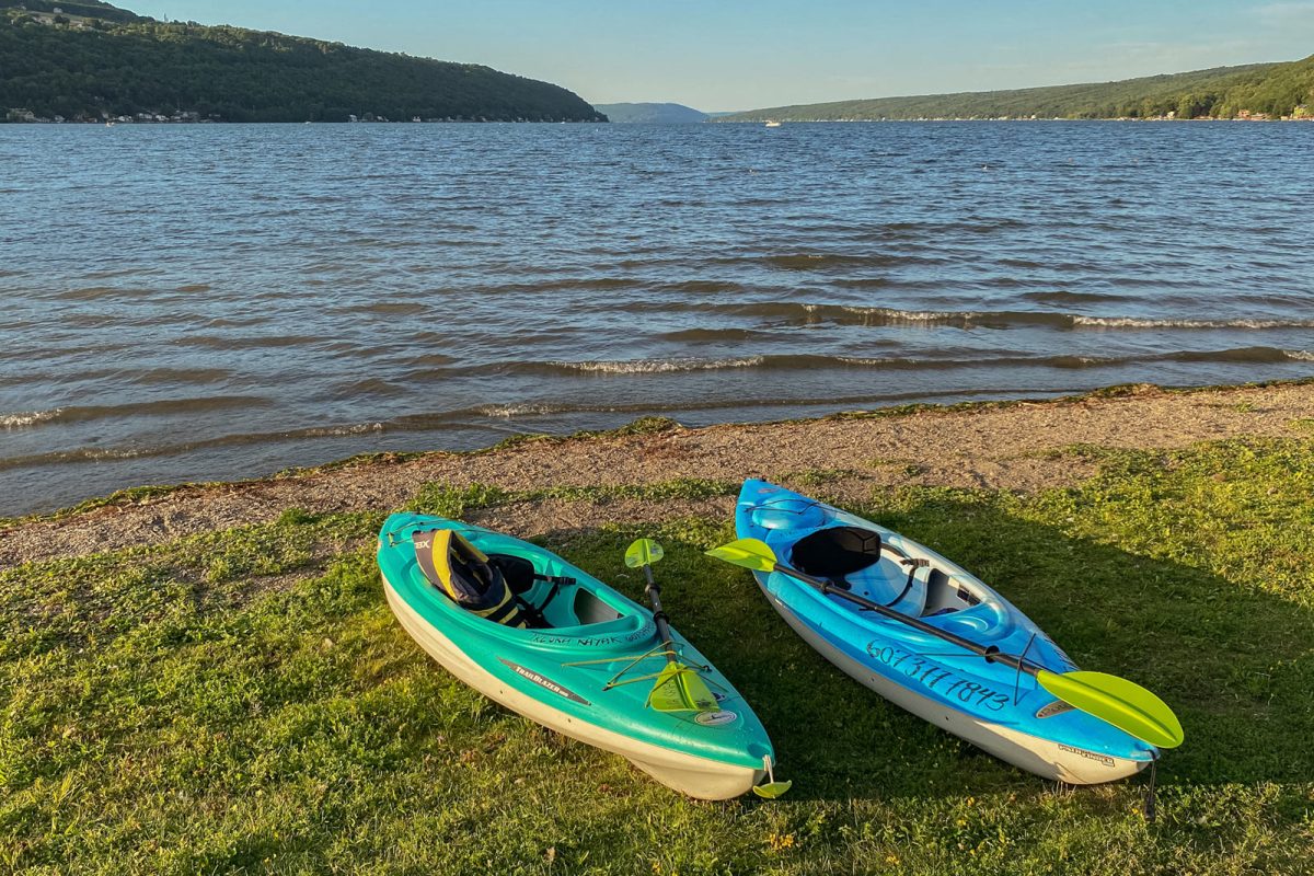 Two kayaks with paddles rest on the shore of a lake. 