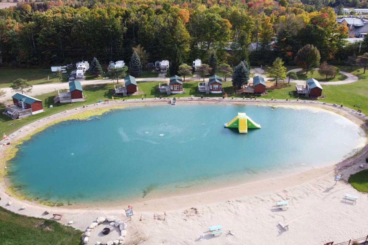 An aerial view of the small body of water and large inflatable water slide at the center. The water is lined with lodging accommodations that are available at Harbour Village Campground and Water Park. 