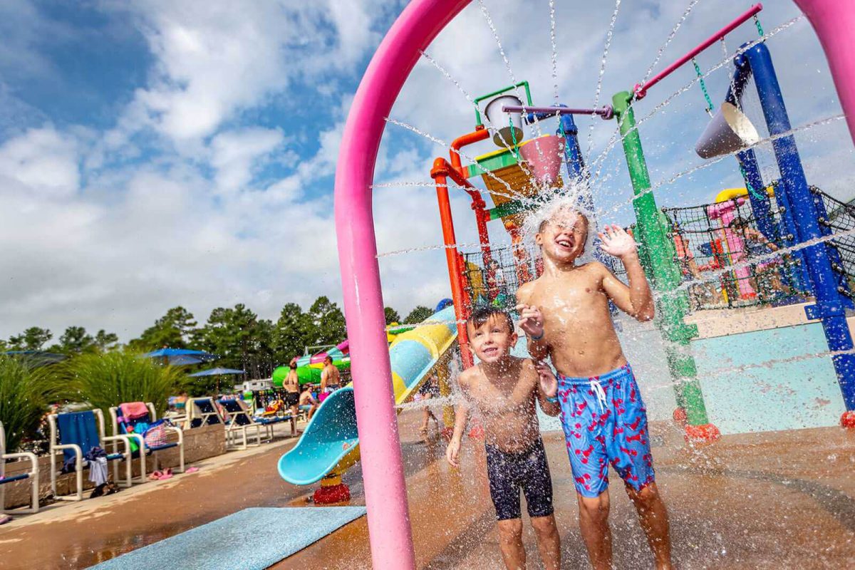 Two boys stand under a water fixture at a campground water park. 
