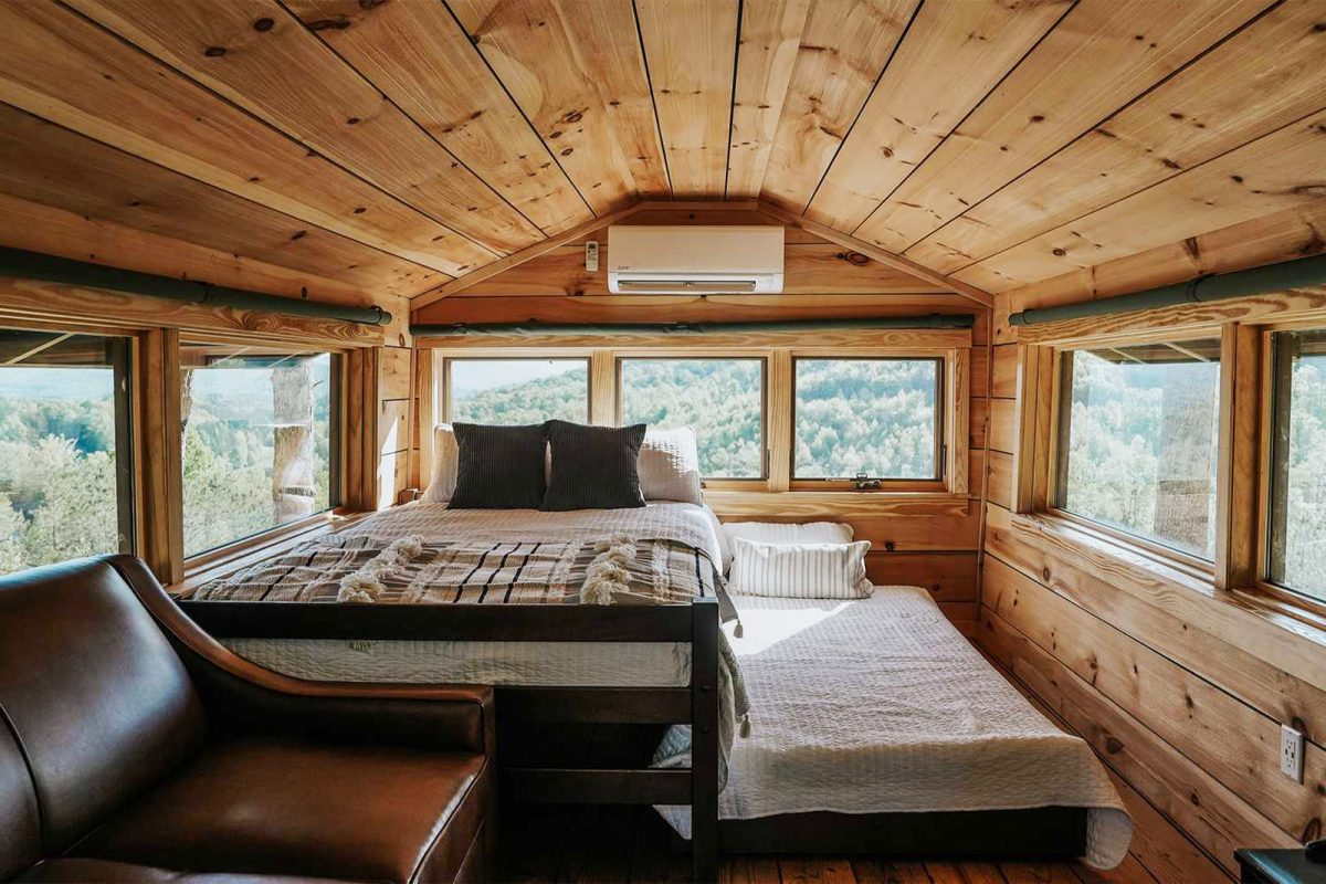 The interior view of a cabin loft with windows on all sides that overlook the surrounding forest at Yogi Bear's Jellystone Park™ Camp-Resort: Golden Valley, one of the favorite campgrounds for stargazing on Campspot. 