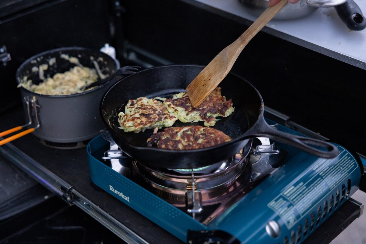 Zucchini and potato fritters in a cast iron skillet on a camp stove. 