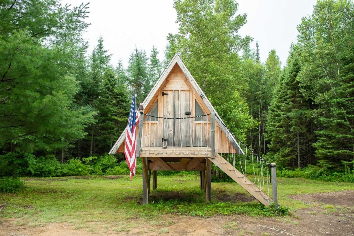 A small a-frame cabin on stilts in the woods at Cottonwood Camping RV park, a campground with cabins in Maine