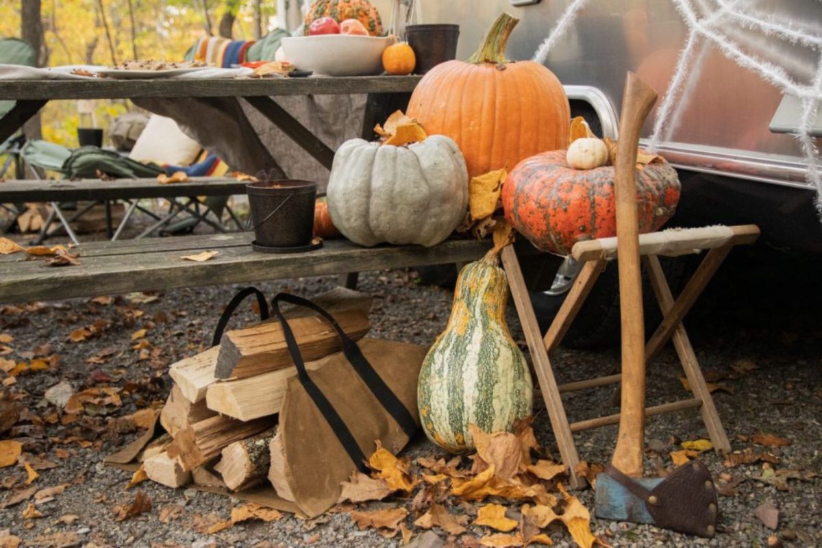Pumpkins and firewood near a picnic table outside of an Airstream 
