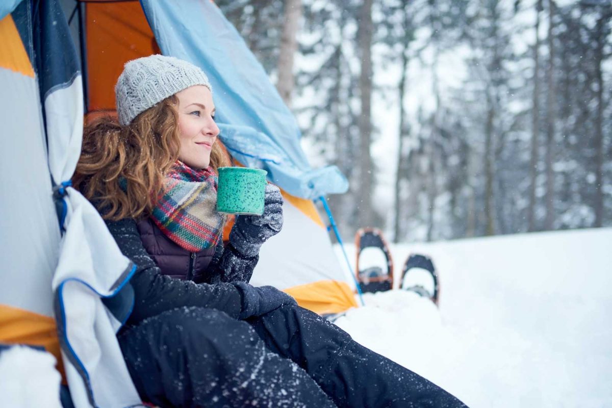 woman enjoying hot drink in tent after snowshoeing