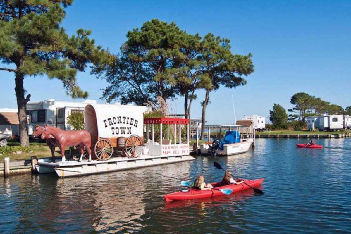 people kayaking on water next to a wagon labeled "Frontier Town"