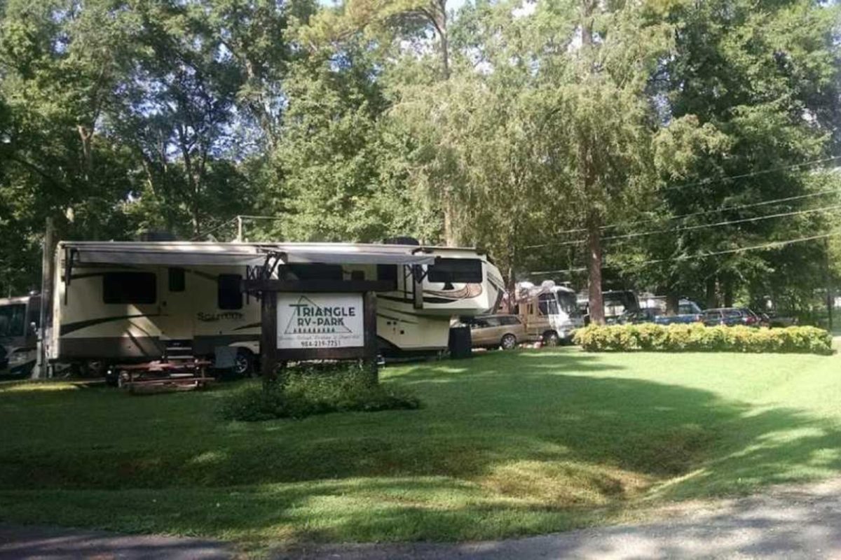 Triangle Park sign in front of parked RV on green field campground
