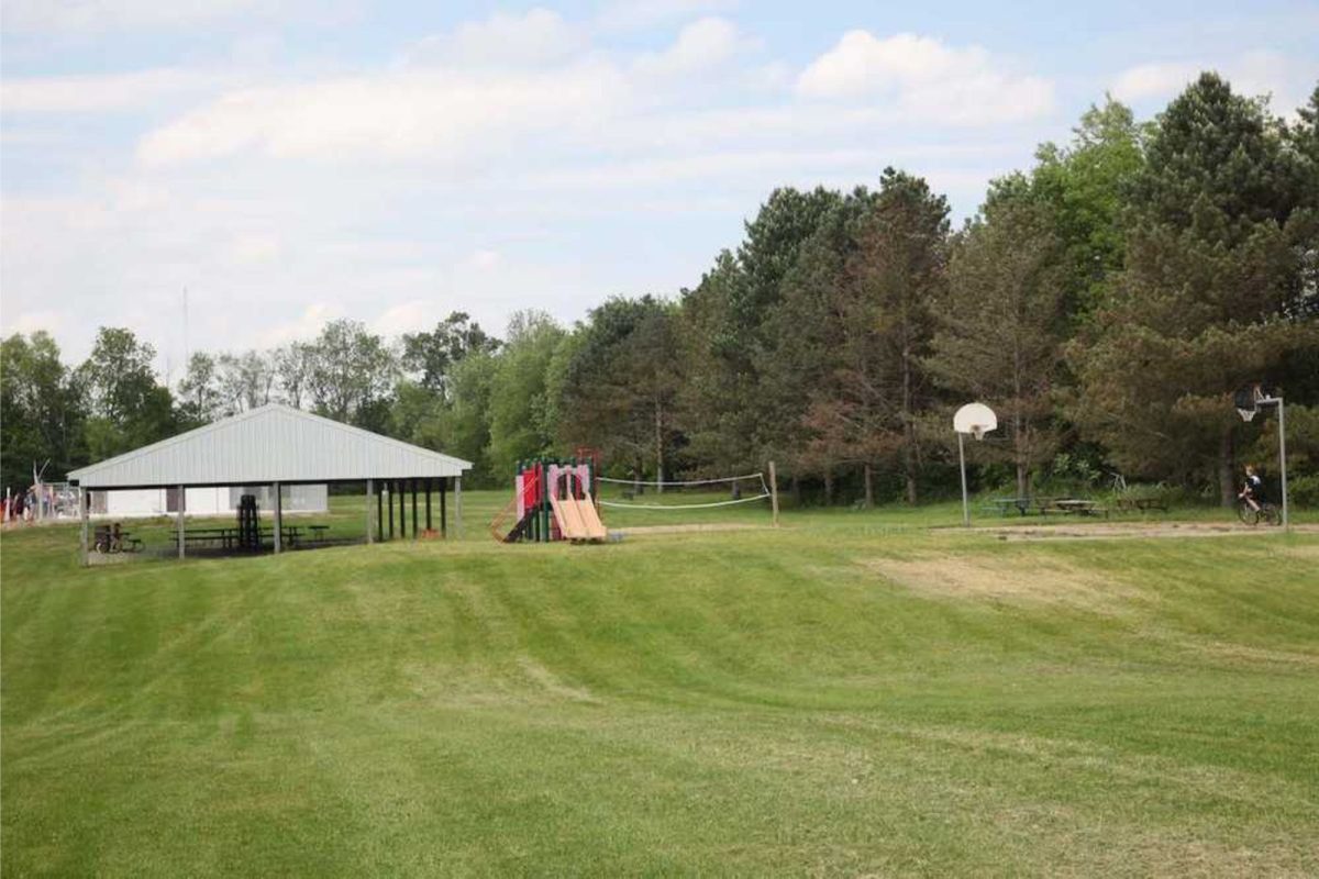 grassy campground field with picnic tables, playground, and basketball court