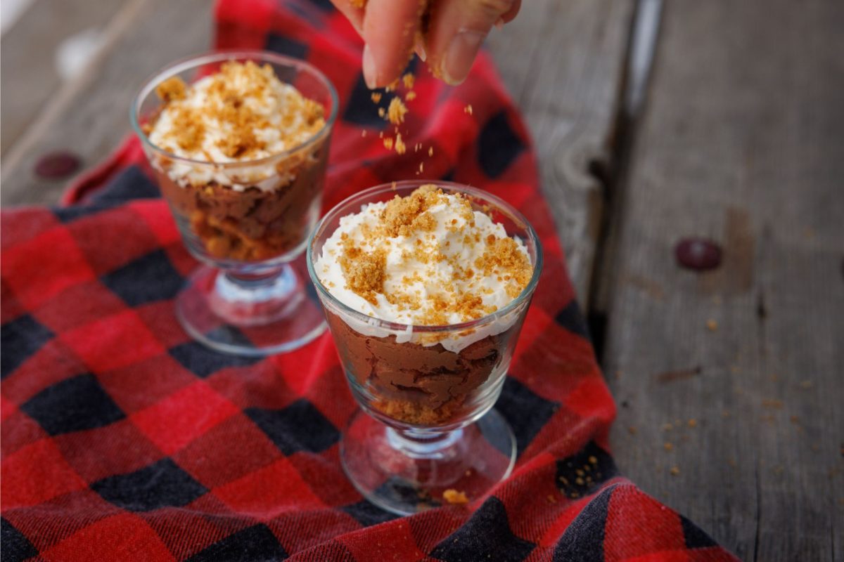 person crumbling graham cracker topping onto cheesecake parfait