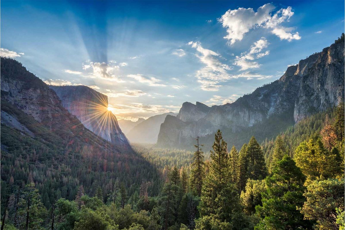 The sun peaks around the grand view of a cliff at Yosemite National Park. 