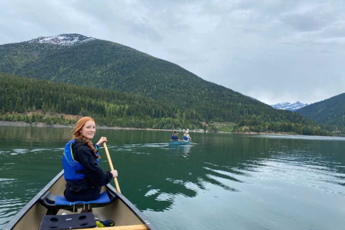 A girl looks back over her shoulder while canoeing with a mountain view in the backdrop. 
