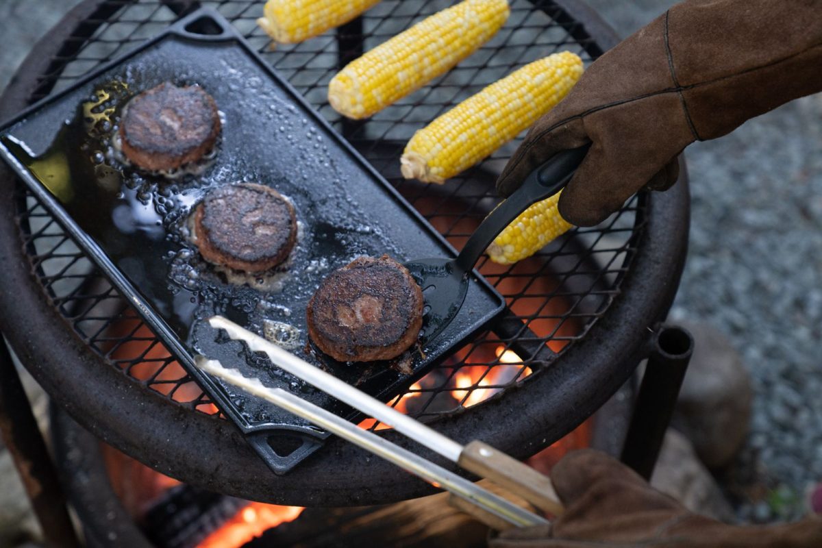 Burgers cooking on a cast iron camping grill plate with corn 