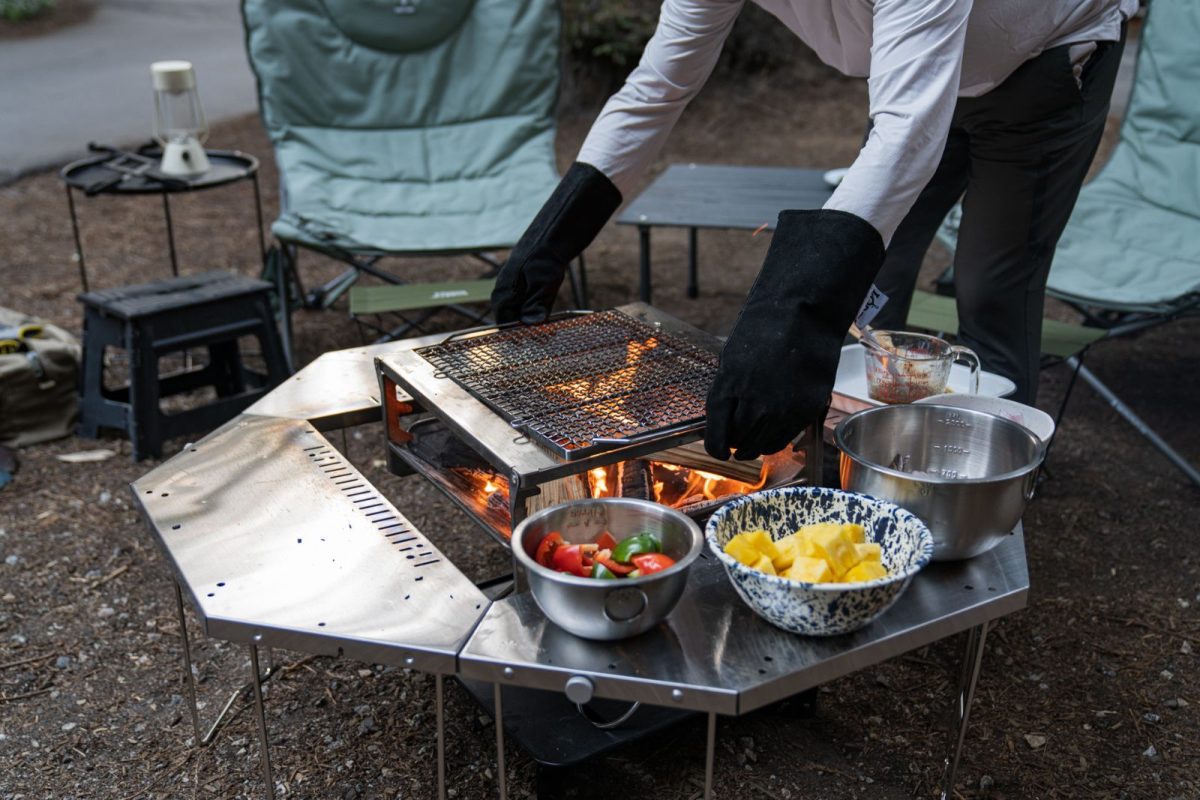 A camper with gloved hands adjusts the grates of her camping grill 