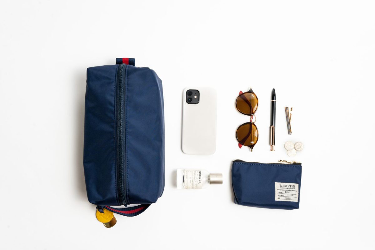 An overhead shot of a Large Dopp Kit in navy blue with a sample of items that might be stored inside such as a phone, sunglasses, and pen. 