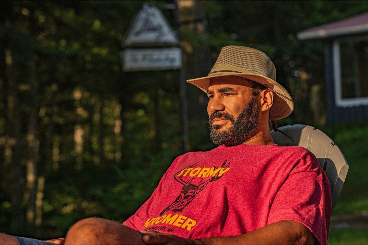 A man sits in the sunshine in a mesh hiker hat. 