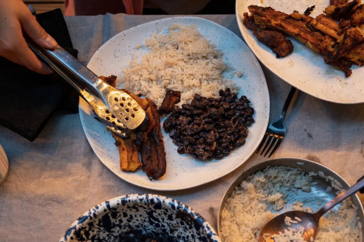 person adding plaintains to a dish with rice and beans