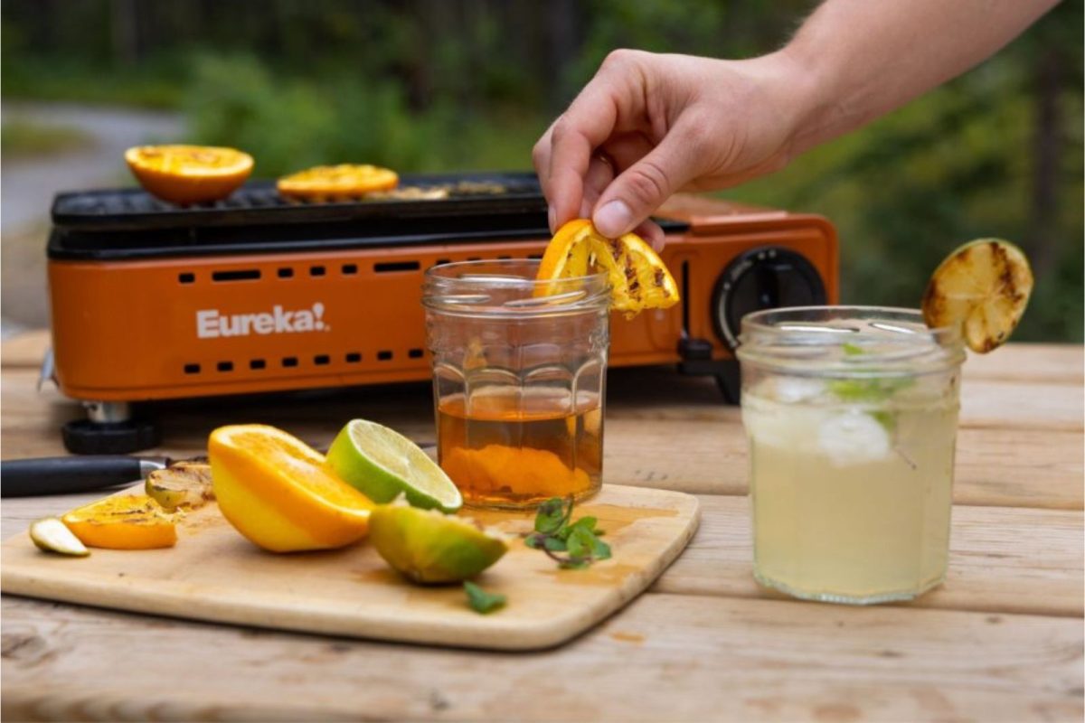 a camper adding a charred orange slice as a garnish to a camping cocktail recipe