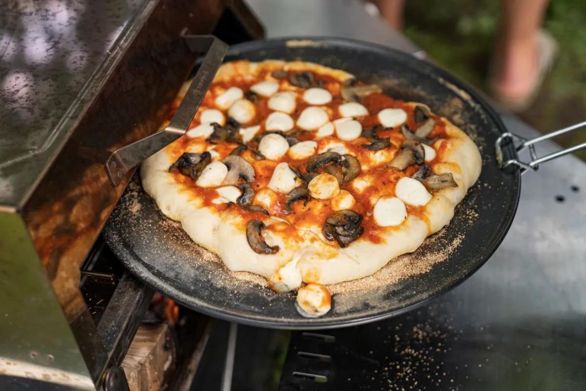 a campfire pizza being pulled out of the oven